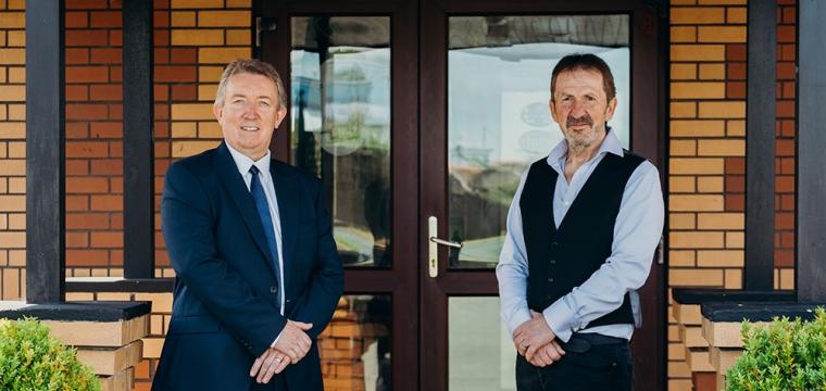 Richard Easton from DBW and Mike Davies, Managing Director (Dale Roads), stood in Front of Dale Roads entrance. Richard is wearing a blue suit with a blue tie and is smiling. Mike is wearing a black blazer on top of a blue shirt.