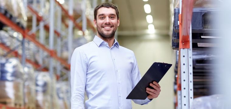 man holding a tablet in warehouse smiling at camera